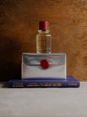 Vanilla veil edp bottle on a silver wrapped perfume box with a red seal, placed on top of a book titled 'The Great Gatsby'.